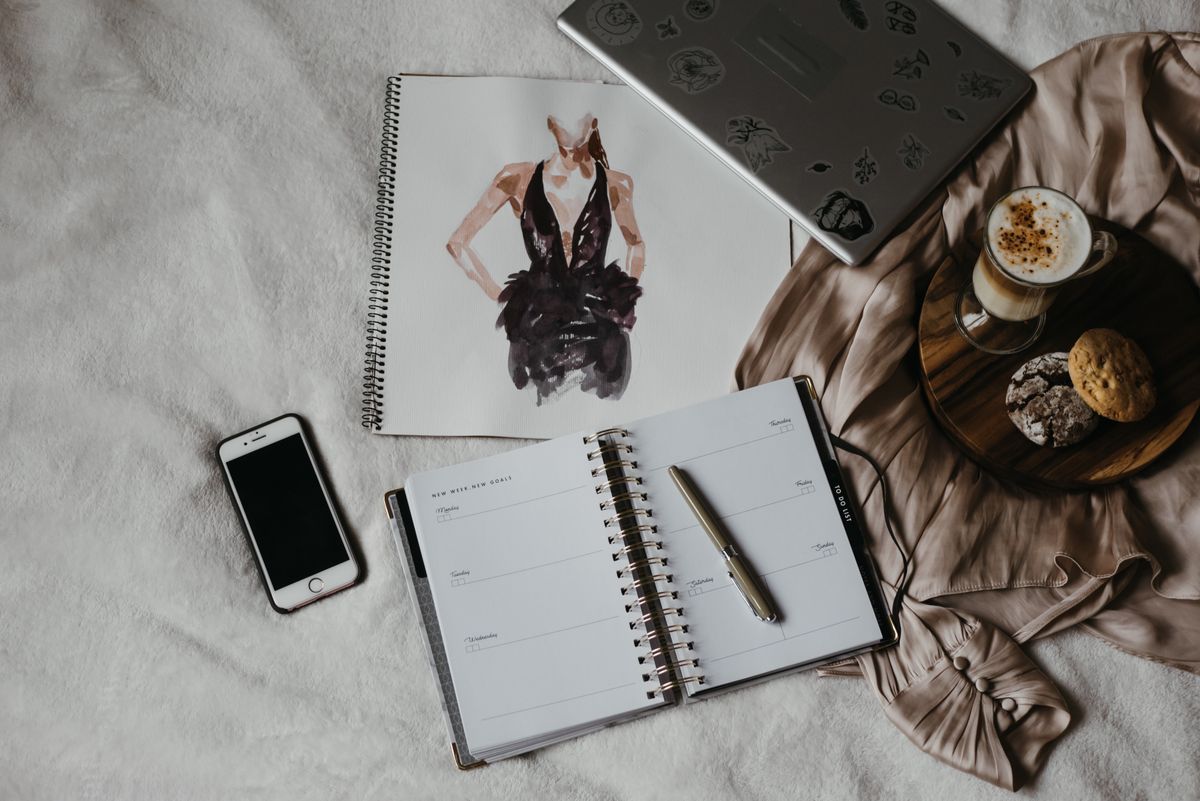 An open notebook beside fashion references and a phone