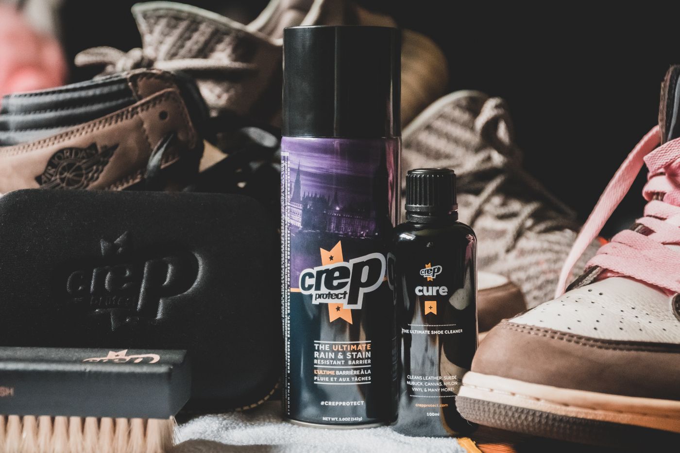 A shoe brush, cloth and care products beside trainers