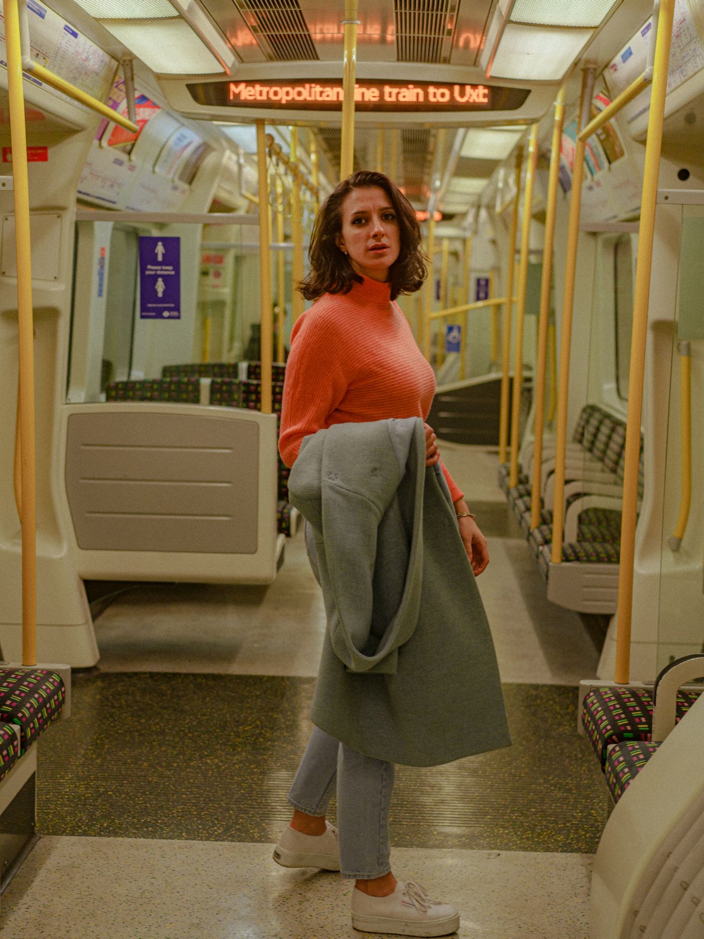 A woman holding her coat over a knitted jumper on a train