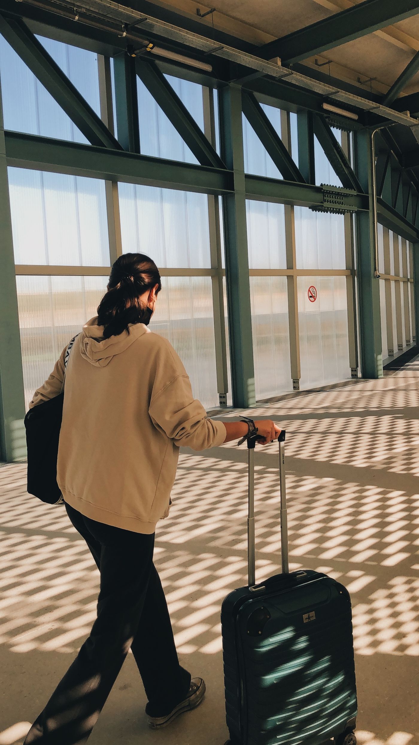 A woman in a light jacket walking through an airport with luggage